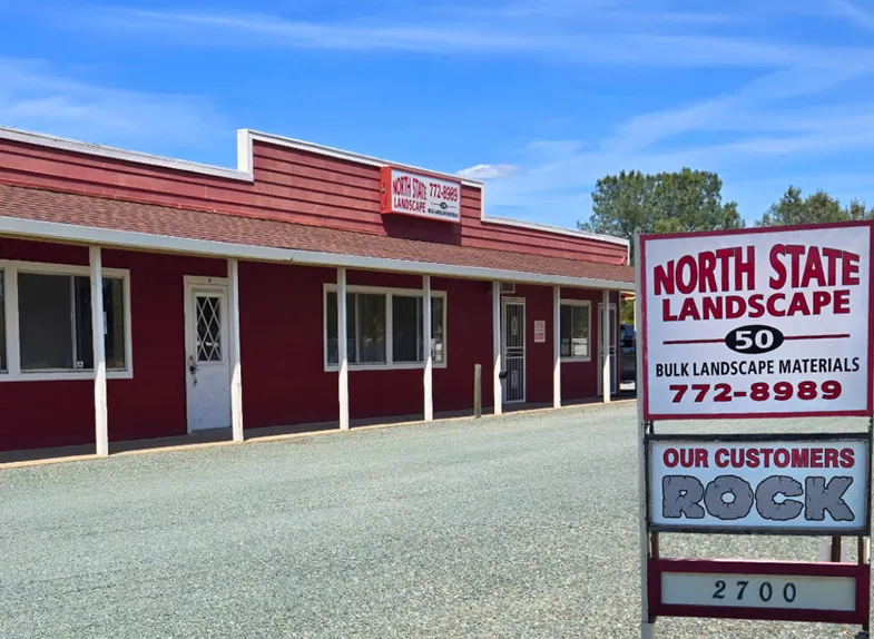 Front view of North State Landscape's red office building in Valley Springs, CA with a sign offering bulk landscape materials and contact information